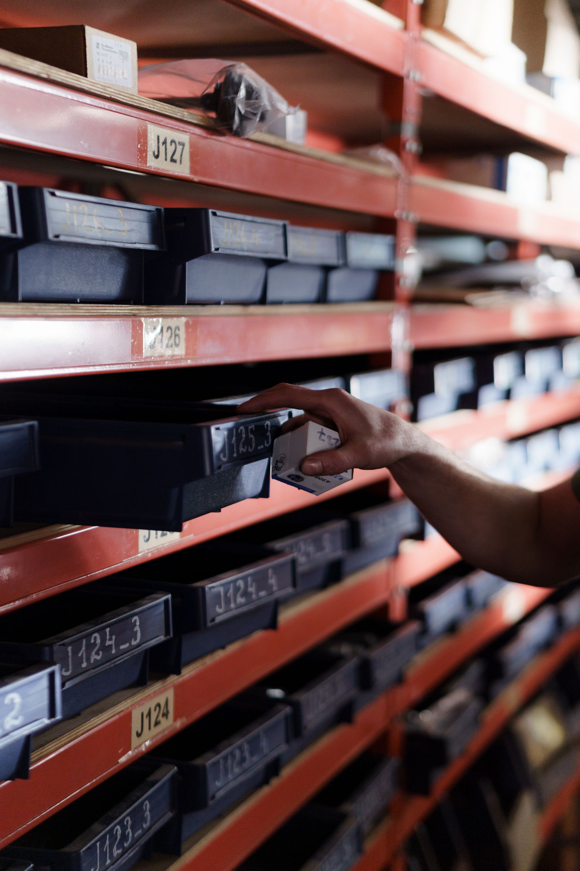A hand selecting a small boxed component from organized warehouse bins